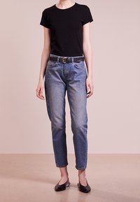 Černé tričko s krátkým rukávem v kombinaci se světle modrými džíny a černým pásem. Oblečení doplňují ploché černé boty. Jednoduchý design, rovný střih.