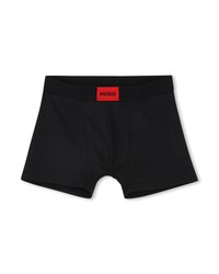 Μαύρα ανδρικά μπόξερ με κόκκινη ετικέτα στη ζώνη μέσης που αναγράφει «HUGO» με μαύρα γράμματα, απλωμένα σε λευκό φόντο.