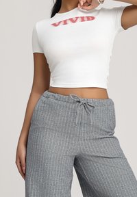 Witte cropped T-shirt met rode "VIVID" tekst, gecombineerd met grijze broek met fijne streep en een trekkoord in de taille.