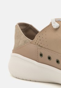 Baskets en cuir beige avec un tissu beige texturé à l'arrière, semelle en caoutchouc blanche et détails perforés. Comprend des lacets et des œillets beiges.