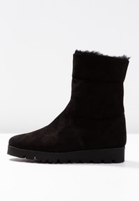 Botas de tobillo de ante negro con un suave forro de piel en la parte superior, puntera redondeada y suela de goma texturizada. Presenta detalles de costura minimalistas.