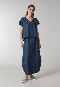 Denim-outfit bestående af en løs V-hals top og en matchende lang nederdel. Stoffet er mørkeblåt med synlige sømme og lommer.