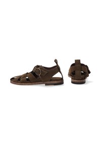 Braune Wildledersandalen mit offenem Design, ausgestattet mit Riemen und einer kreisförmigen Schnalle; flache Sohle mit einem hellbraunen Rand.