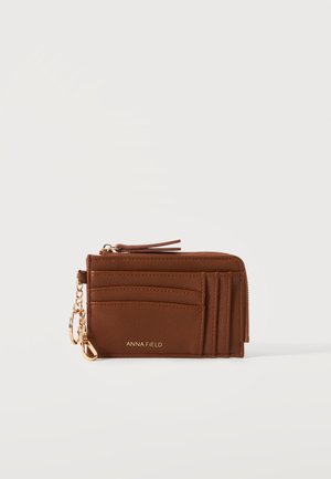 Portefeuille en cuir marron avec plusieurs emplacements pour cartes, une poche zippée, une attache porte-clés dorée et le logo "Anna Field" à l'avant.
