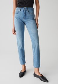 Jeans azzurri chiari con taglio dritto, vita alta e sottili scoloriture. Abbinati a décolleté nere a punta. Texture del denim liscia.