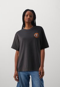 Black cotton t-shirt with a crew neck and short sleeves; features an orange graphic logo on the left chest. Classic fit.