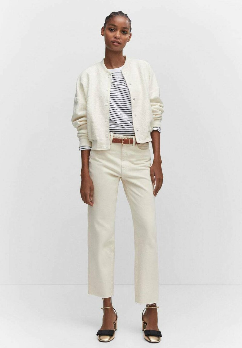 Helle Creme Bomberjacke aus strukturiertem Stoff, gestreiftes Shirt in Weiß und Marineblau, cremefarbene weit geschnittene Hose und schwarze High Heels mit Schleifenakzenten.