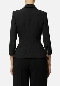 Blazer nero su misura con silhouette aderente, cuciture strutturate e dettagli con cerniere sulle maniche. Tessuto liscio, design minimalista.