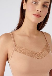 Canottiera nuda con pizzo, caratterizzata da un design a V. Realizzata in materiale morbido, presenta spalline regolabili e una texture liscia.