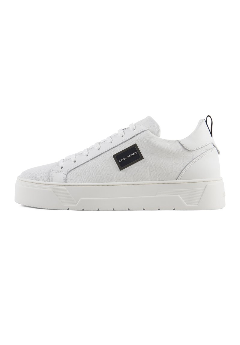 Hvit sneakers med et teksturert krokodillemønster, glatt syntetisk overdel, flat såle, og en svart logoakcent på siden.