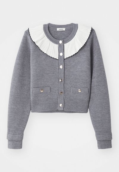 Γκρίζα κάρντιγκαν με πλισέ λευκό γιακά, κουμπιά μπροστά, δύο μπροστινές τσέπες και ριπ μανίκια και στρίφωμα.