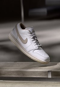 Fehér, alacsony szárú bőr sneaker bézs akcentusokkal, strukturált fűzőkkel, perforált orral és gumitalppal, amelyen látható varrások találhatóak.
