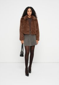 Brūns mākslīgās ādas īsais mētelis ar apkakli, apvienots ar brūnu ribotu topu, pelēku mini svārku, melnām zeķubiksēm un melniem augstiem papēžiem, turot melnu somu.