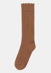 Brune strikkede knestøttestrømper med mønster, bølget kant og ribbestrikket design. Materialet ser mykt og elastisk ut.