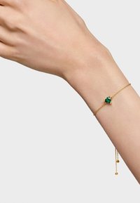 Bracciale in catena d'oro con un centro di pietra verde, con link di catena delicati e lunghezza regolabile. Il bracciale è caratterizzato da piccole perline pendenti.