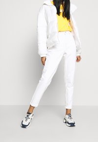 Chaqueta puffer blanca, camiseta amarilla y jeans blancos de pierna recta. El calzado tiene acentos en azul y blanco. Texturas suaves en todo.