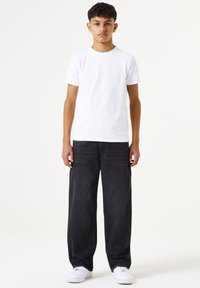 Camiseta blanca de algodón combinada con jeans de mezclilla oscura, con un ajuste relajado. Los jeans tienen un corte recto y están estilizados con zapatillas blancas.