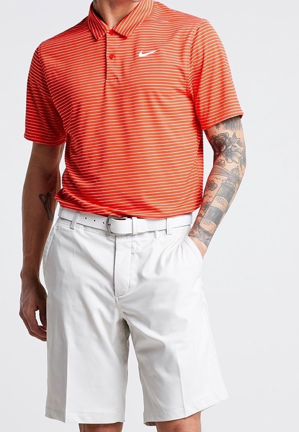 Röd och vit randig polo skjorta med krage och en Nike-logotyp, i kombination med vita shorts som har ett bälte, i stående pose.