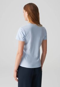 Helles blaues Kurzarm-T-Shirt mit einer figurbetonten Passform. Glatte Textur, runder Halsausschnitt und keine sichtbaren Logos oder Muster. Dunkle Hosen ergänzen das Outfit.