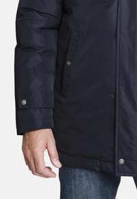 Parka aislante de color azul marino con un acabado texturizado, que cuenta con botones a presión, bolsillos laterales y un diseño de mangas con puños.