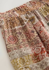 Tissu ample avec une ceinture élastique, présentant un motif patchwork de dessins floraux et ornementaux dans des tons de brun, rouge, vert et beige.