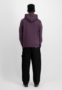 Hanorac violet cu glugă, cu mansete cu nervuri, asortat cu pantaloni cargo negri, largi, cu buzunare laterale. Design simplu și casual.
