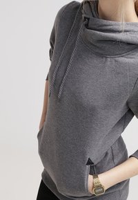 Harmaa huppari, jossa on huppu, säädettävät kiristysnauhat ja sivutaskut. Pehmeästä kankaasta valmistettu, rento istuvuus ja lyhyet hihat.