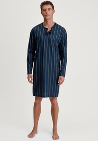 Camicione a maniche lunghe in tessuto blu scuro con righe verticali e un sottile motivo geometrico. Presenta un colletto con bottoni e una tasca sul petto.