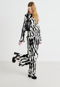 Giovane donna che indossa un top e pantaloni coordinati con stampa astratta in bianco e nero, tacchi alti neri e porta una borsa a tracolla nera.