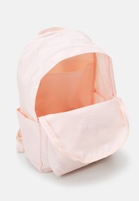 Růžový látkový batoh s překlopnou klopnou, velkým vnitřním prostorem a bočními kapsami. Hladký povrch s minimalistickým designem.