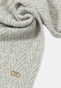 Tessuto grigio chiaro lavorato a maglia con un sottile motivo a zigzag e piccoli paillettes, con una piccola targhetta ovale dorata con un logo.