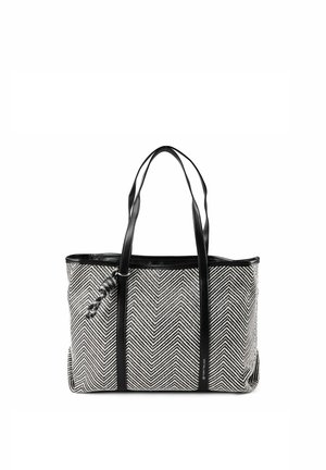 Schwarz-weiß gemusterte Tasche im Fischgrätmuster mit langen schwarzen Trägern und einem kleinen geflochtenen Accessoire auf der einen Seite.