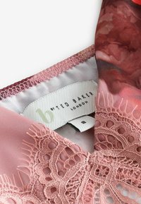 Haină Ted Baker cu un model floral, material roz deschis și detalii complicate din dantelă. Include o etichetă pentru îngrijirea materialului.