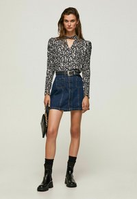 Blusa a fantasia floreale con maniche lunghe e scollatura a taglio, abbinata a una gonna A-line in denim blu e stivaletti neri alla caviglia.