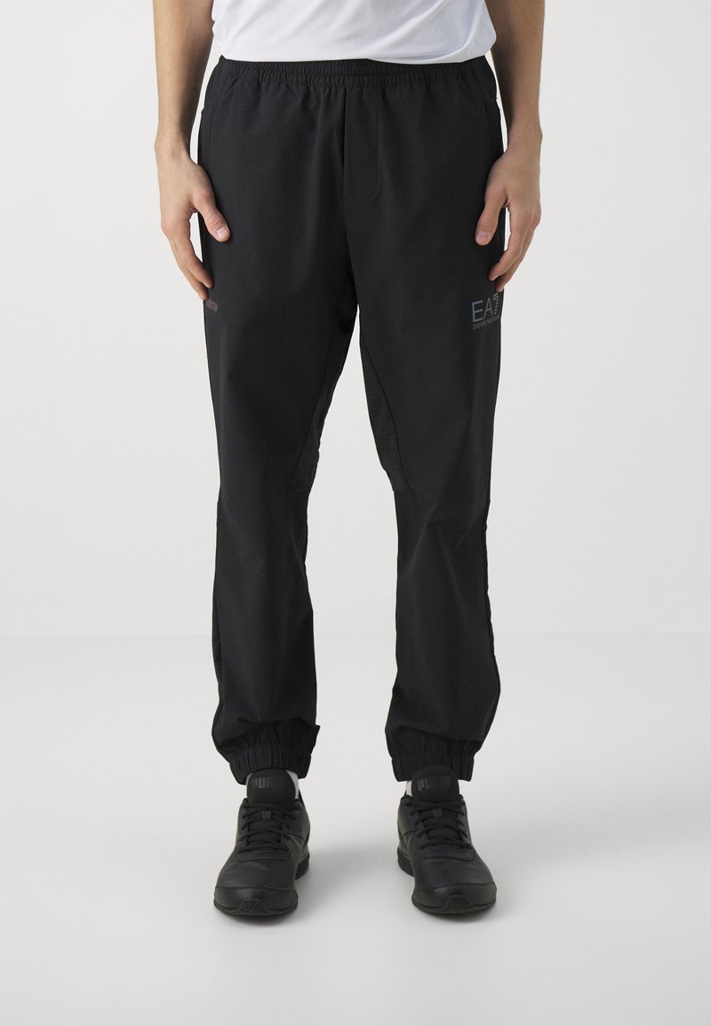 Black athletic pants with an elastic waistband, tapered fit, and cuffs. Features side pockets and a small logo on the thigh. Lightweight material.