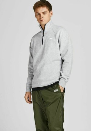 Sudadera de forro polar gris claro con diseño de media cremallera y un pequeño logo en el pecho, combinada con pantalones oscuros verdes, ligeros y con cintura elástica.