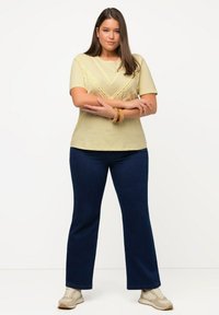 T-shirt giallo chiaro a maniche corte con un design testurizzato a V; abbinato a jeans svasati blu scuro e sneakers beige. Tessuto morbido.