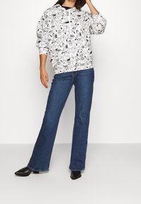 Felpa bianca con una stampa sportiva giocosa, abbinata a jeans blue flare e stivali neri a punta. Tessuto misto cotone, vestibilità comoda.