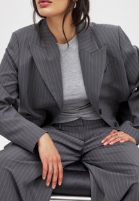 Pelēkas svītrainas žaketes ar platām atloks, pārī ar pieguļošu pelēku augšu. Bikses ir augsti jostasvietā, veidojot piegriezuma siluetu.