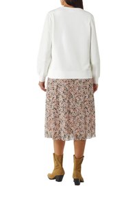 Witte sweatshirt met lange mouwen, gecombineerd met een bloemenrok tot de knie met roze en zwarte accenten, en bruine haklaarzen.