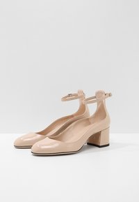 Scarpe con tacco a blocco in pelle verniciata beige, con punta arrotondata e cinturino alla caviglia. Superficie liscia con una finitura lucida, che offre un design moderno.