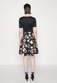 Haut noir à manches courtes associé à une jupe noire évasée ornée de motifs floraux dorés. La jupe a une taille cintrée et s'évasent vers l'extérieur.
