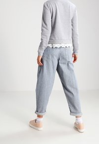 Ljusgrå sweatshirt med spetsdetaljer, tillsammans med löst sittande blårandiga jeans med uppvikta avslut och ljusbeige sneakers.