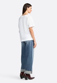 Hvid kortærmet top med en rund halsudskæring, parret med lysblå bred-bene jeans og mørkebrune hælede ankelstøvler.