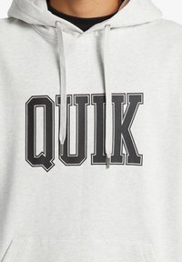 Lys grå hættetrøje lavet af blød bomuldsblanding med et stort sort "QUIK" logo. Har justerbare snore og en kengurulomme.