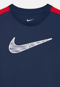 Marineblaues Sport-T-Shirt mit Rundhalsausschnitt, roten Schulterakzenten und einem großen weißen Nike-Swoosh-Logo mit gestreiftem Detail.