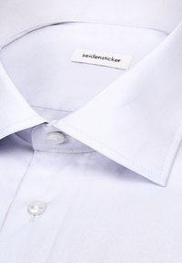 Chemise blanche habillée avec col pointu et boutons blancs, montrant une étiquette cousue avec le nom de la marque seidensticker à l'intérieur du col.