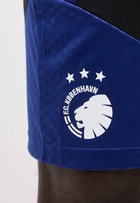Μπλε αθλητικό σορτς με λευκό λογότυπο FC København, που απεικονίζει κεφάλι λιονταριού και τρία αστέρια πάνω του στο μηρό.