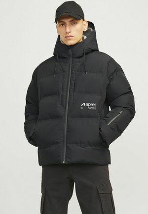 Chaqueta acolchada negra con cuello alto, cierre de cremallera frontal y logo en el pecho. Cuenta con puños elásticos y bolsillos laterales con cremallera. Diseño texturizado acolchado.