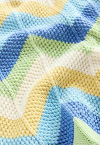 Couverture en tricot présentant un motif ondulé dans des couleurs pastel : bleu, vert, jaune et crème, avec une surface texturée et une finition douce.